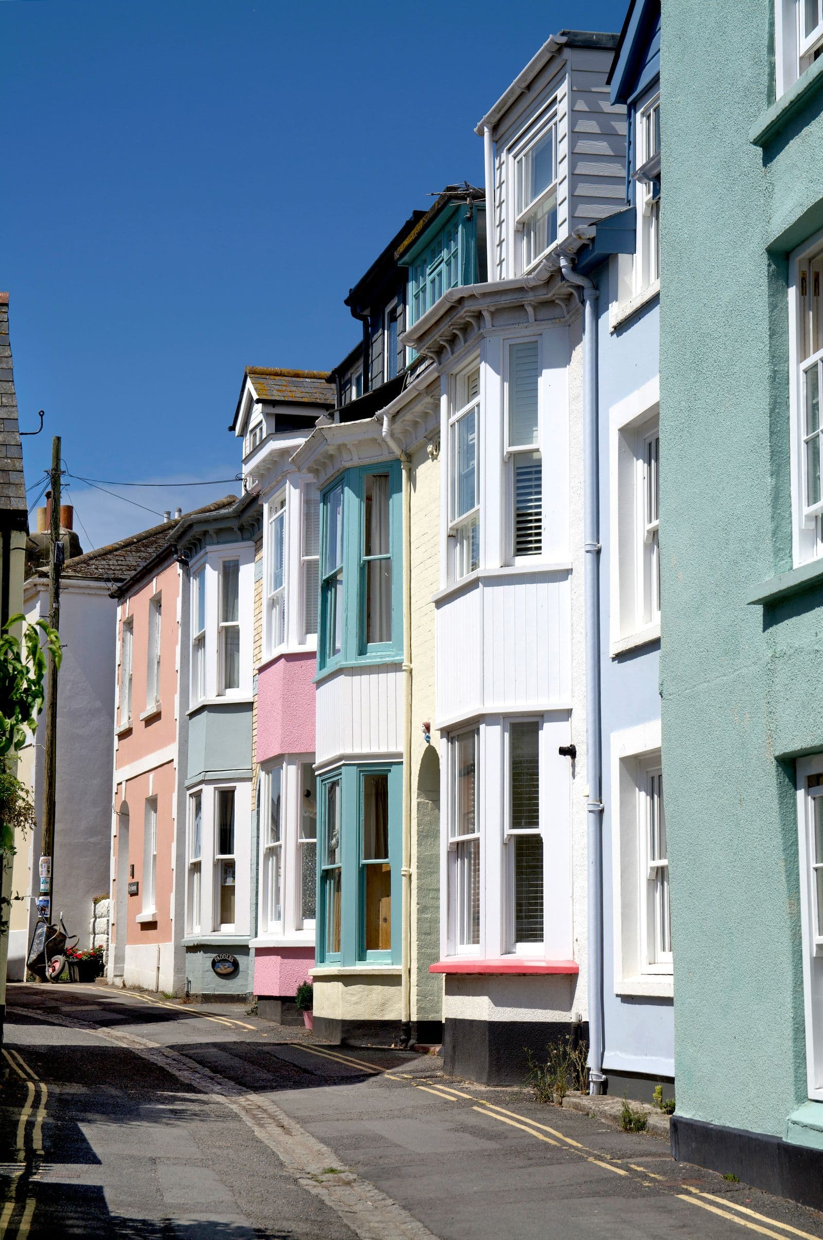 A row of pastel-painted Victorian seaside terraced houses with bay windows and sash windows